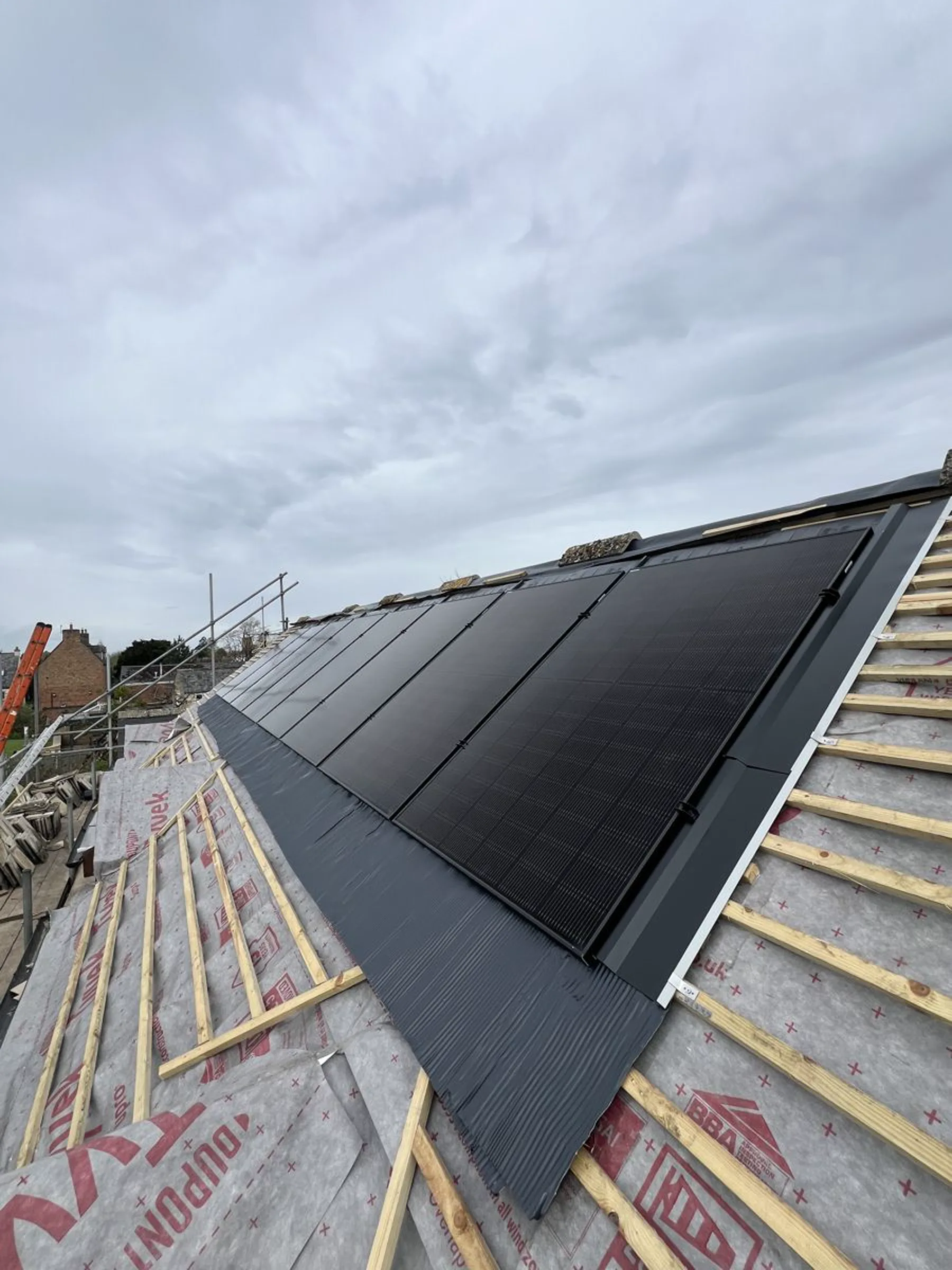 Solar panels being fitted to a roof under an open sky, mid-installation